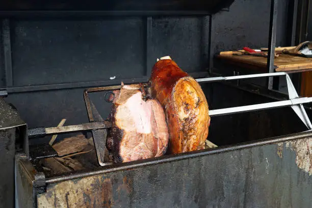 Photo of Pork leg, knuckle is fried on a spit on fire. European holiday Czech traditional dish. Grilled pork meat on the grill.