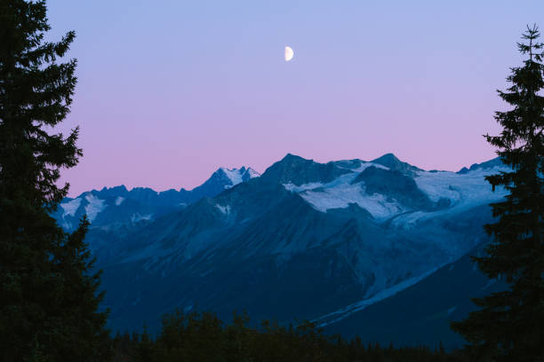Alaskan mountains with half moon and pink skies after sunset during blue hour