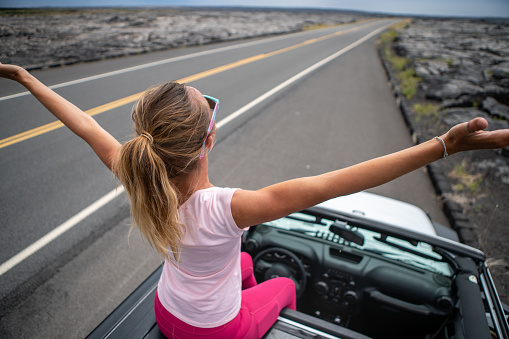 Girl sitting on roof of vehicle looking at volcanic landscape covered by lava