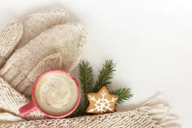 pink mug with foamy drink and ginger Christmas star, mittens and scarf on a table top view