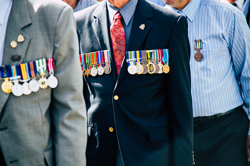 A formed body of old military veterans march past the crowd during the Cooroy-Pomona ANZAC Day parade. The man in the foreground proudly wears the golden Order of Australia Medal (OAM) along with campaign medals from The Vietnam War, the Infantry Combat Badge (ICB) and general Defence service medals. The man marching behind him wears his personal medals on his right breast and World War 2 service medals on his left side.