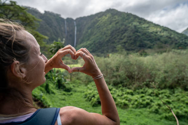 hiking woman making heart shape with hands on waipio valley, hawaii - hamakua coast imagens e fotografias de stock