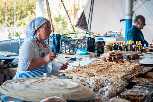 Bodrum, Turkey - August 23, 2019. Beautiful Turkish woman makes and sells cakes, pita bread, pastries in an open-air market.