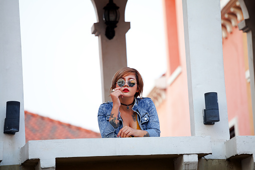 Sad looking young blond thai girl with sunglasses in jeans jacket on bridge of building