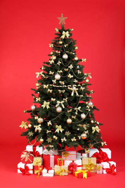 istock Christmas fir tree with ornaments and gift boxes on red background 1192251270