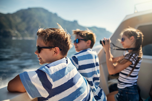 Two little boys and a teenage girl enjoying ferry boat ride to the famous city of Amalfi in Campania, Italy. The girl is taking photos.\nNikon D850