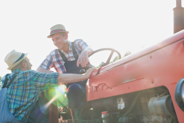 istock Mature farmer talking to senior farmer while sitting on tractor in field 1192253127
