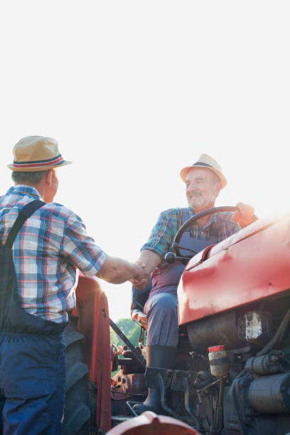 istock Senior farmer shaking hands with mature farmer while sitting on tractor 1192253862