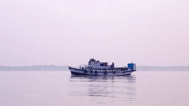 A Small Commercial Fishing trawler (nautical vessel) on river inland water before heading out to Bay of Bengal. Late evening view with rural background. Fishing hub, Digha Mohona, West Bengal, India.