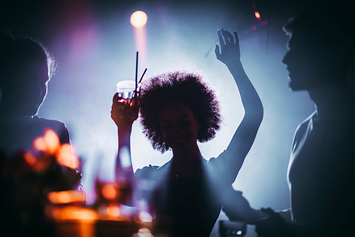 Silhouette of a funky girl holding up a cocktail and dancing to the tune in a night club.
