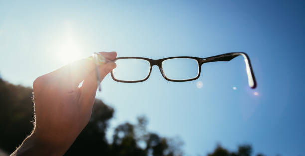 istock Hand holding glasses outdoors, blue sky, sunbeam with lens flares 1192258596