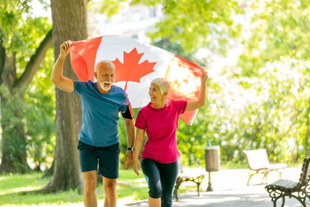 Senior Active Athletes are Waving Canadian Flag and Jogging in the Public Park. Proud Canadians with the National Flag in Nature.