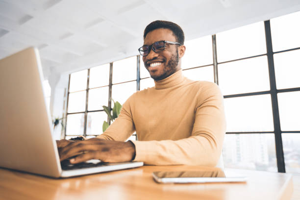 istock Smiling black guy at flexible office typing on keyboard 1192259193
