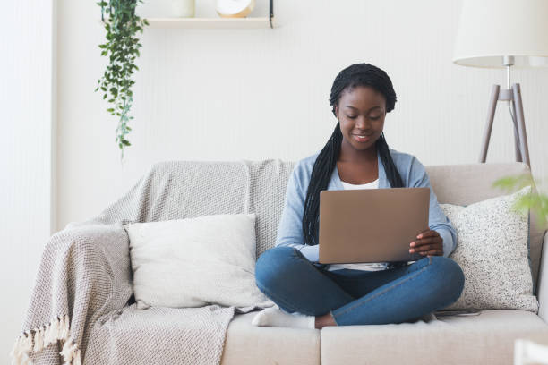 istock Black millennial woman working with laptop computer on sofa at home 1192259954