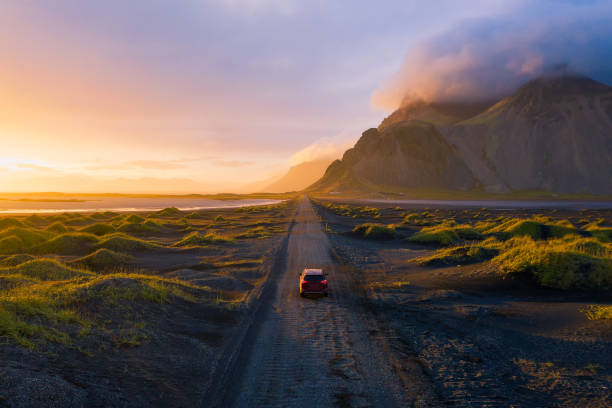 carretera de grava al atardecer con la montaña vestrahorn y un coche de conducción, islandia - vibrant color summer rock cliff fotografías e imágenes de stock