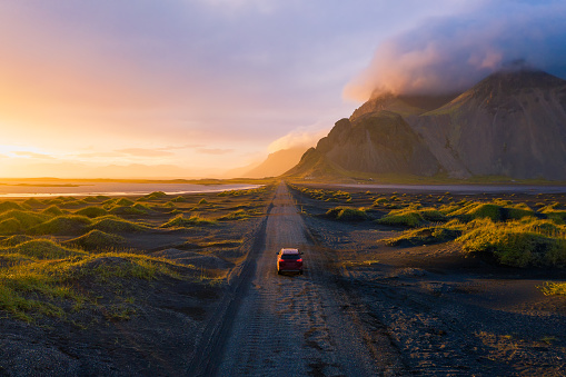 Gravel road at a golden Sunset with Vestrahorn mountain in the background and a car driving the road in Iceland