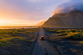 Gravel road at sunset with Vestrahorn mountain and a car driving, Iceland