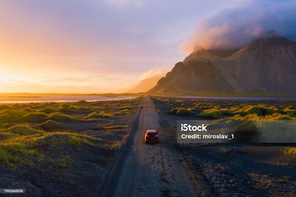 Gravel road at sunset with Vestrahorn mountain and a car driving, Iceland Gravel road at a golden Sunset with Vestrahorn mountain in the background and a car driving the road in Iceland Car Stock Photo