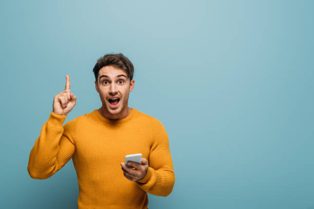 istock surprised man using smartphone and pointing up, isolated on blue 1192266952