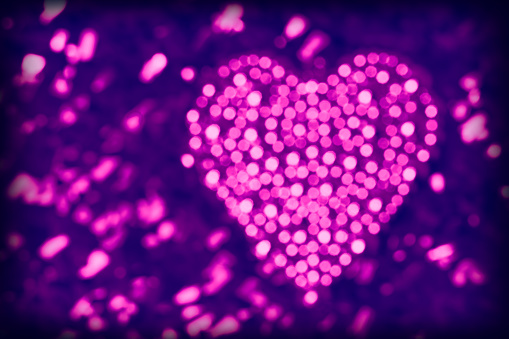 Heart made of purple defocused lights on a glittering background. Beautiful bokeh, space for copy.