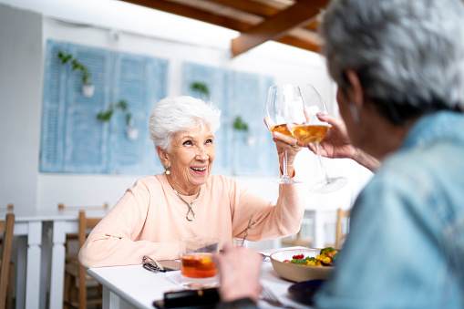 Senior couple celebrating retirement outdoor.  White man and woman. Holding white wine glasses with tropical garden in background. Holding close.