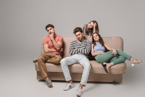 bored and pensive friends sitting together on sofa on grey