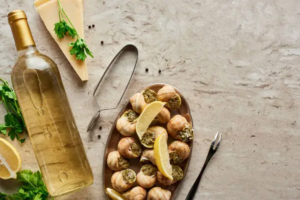 top view of delicious served escargots near bottle of white wine and parmesan on stone background