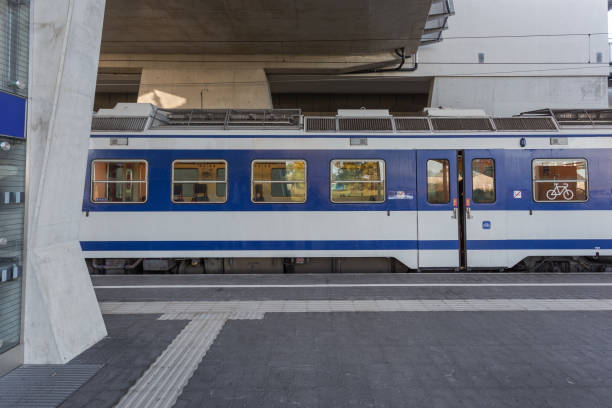 Blue and white train waiting on passengers at an outdoor train stop on a clear day