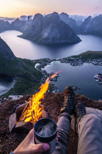 男は火のそばにいて、お茶を飲みながら、レーヌブリングゲンの上に座る - lofoten scandinavian norway nature ストックフォトと画像