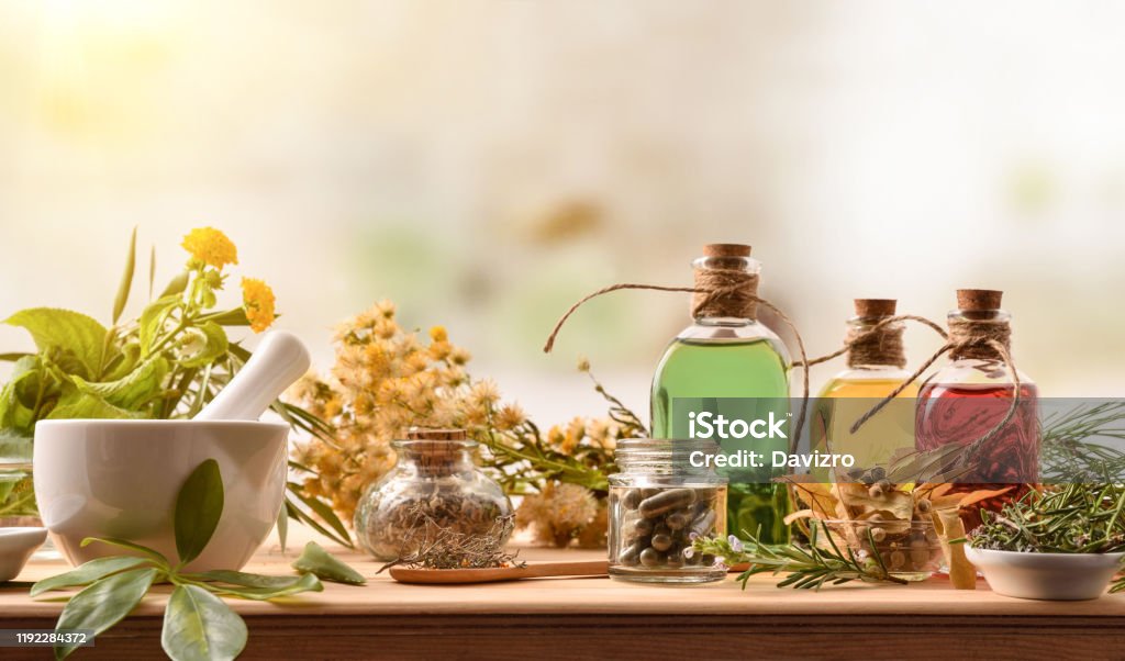Composition of natural alternative medicine with capsules essence and plants Composition of natural alternative medicine with capsules, essence and plants on wooden table in rustic kitchen. Front view. Horizontal composition. Herbal Medicine Stock Photo
