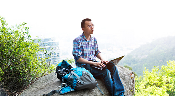 Hiker sitting on a rock and working on laptop.
