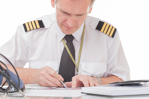 Airline pilot wearing shirt with epaulets and tie filling in filling in and checking papers logbook and checking papers and weather forecast
