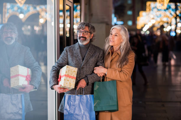 Mature couple walking in the evening and shopping gifts for New Year Mature couple walking through the city at the evening and shopping presents for Christmas. window shopping at night stock pictures, royalty-free photos & images