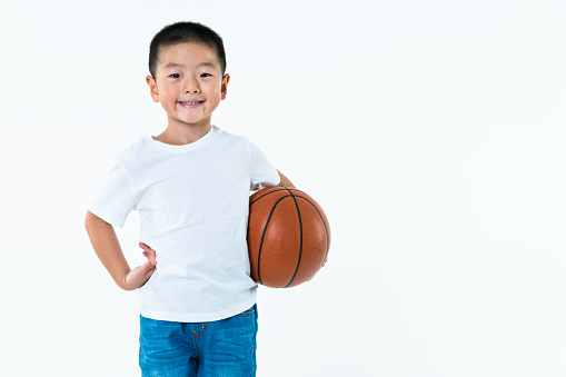 Little asian boy holding a basketball against white background.