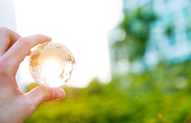 hand holding glass globe with grassy background - transparent holding glass focus on foreground imagens e fotografias de stock