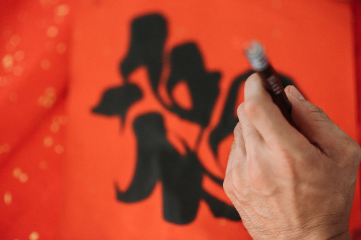 top view of hands writing chinese calligraphy characters with black ink on red colour paper