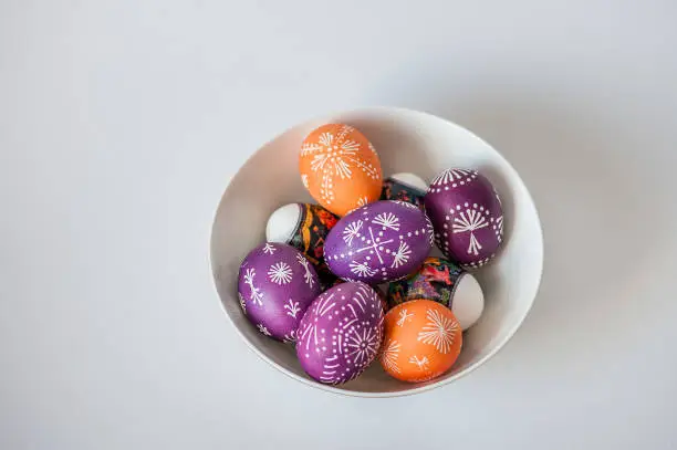 Photo of Orange and purple Easter eggs in a plate on white background.