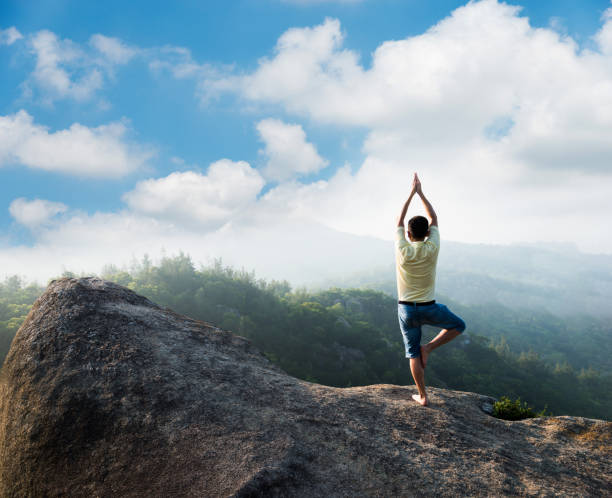 Asian man doing yoga on mountain peak cliff.