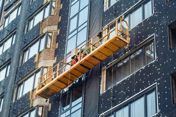 Photo of Suspended construction craddle near wall of hightower residentaial building with insulation and ventilated facade on construction site. Engineering urban background