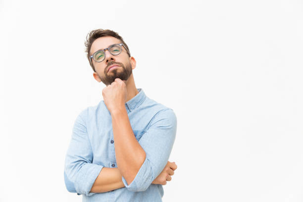 istock Pensive guy in eyewear touching chin and looking away 1192311945
