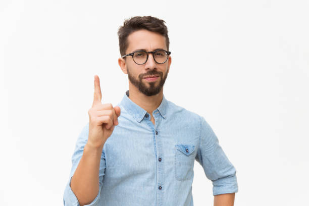 Positive friendly guy having idea Positive friendly guy having idea and pointing index finger up. Handsome young man in casual shirt and glasses standing isolated over white background. Advertising concept index finger stock pictures, royalty-free photos & images
