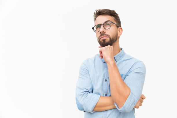 Pensive customer thinking over special offer Pensive customer thinking over special offer, touching chin, looking up. Handsome young man in casual shirt and glasses standing isolated over white background. Advertising concept reflection stock pictures, royalty-free photos & images