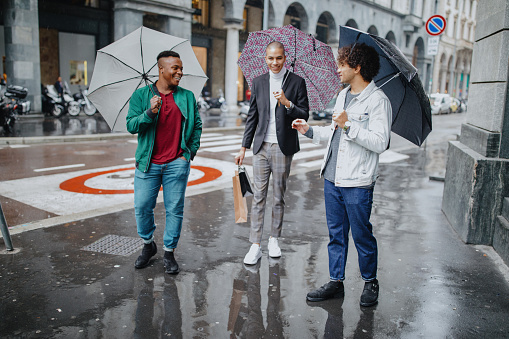 Three young men with shopping bags walking in the rain holding umbrellas