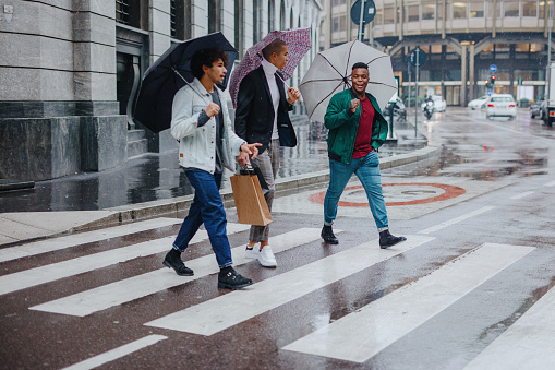 Three young men with shopping bags walking in the rain holding umbrellas