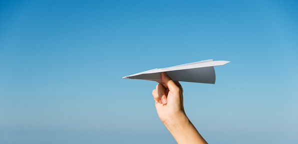Hand holding a paper airplane against blue sky background.