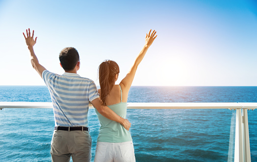Young couple with arms around enjoying the view on cruise ship