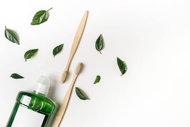 Oral care products. Mouthwash, two wooden bamboo eco friendly toothbrushes, green leaf on white background. Teeth hygiene concept. Flat lay, copy space stock photo