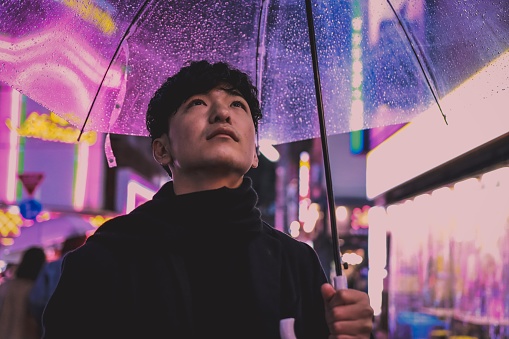 Asian young man is having an umbrella under the rain in the night.