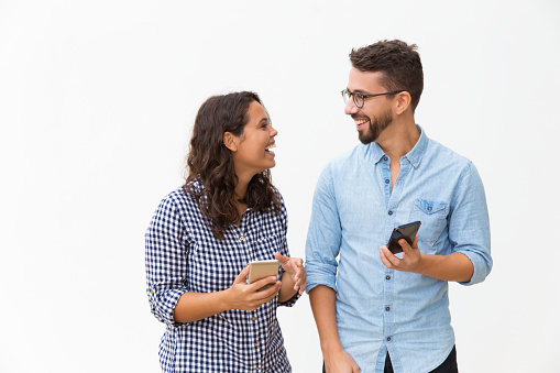 Happy excited couple with smartphones discussing awesome news. Young woman in casual and man in glasses in glasses posing isolated over white background. Mobile app or good news concept