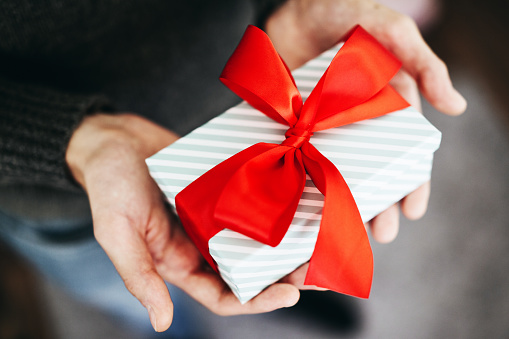 Young man holding gift with red ribbon. Closeup. Opening gift.